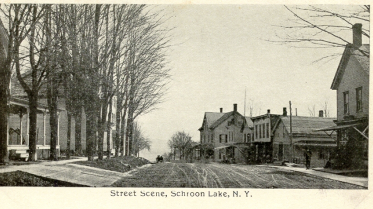 An antique postcard shows a black and white image of a small town's Main Street in the early 20th century.